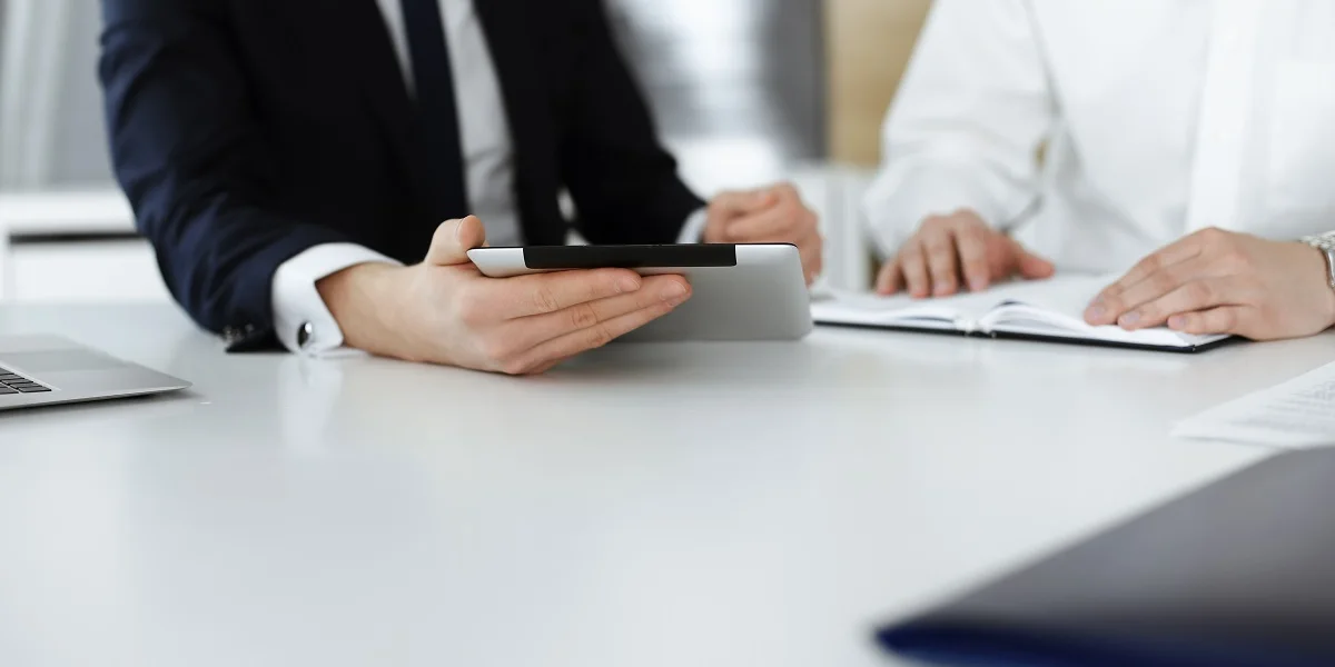 Two officials at a meeting table, one holding a tablet